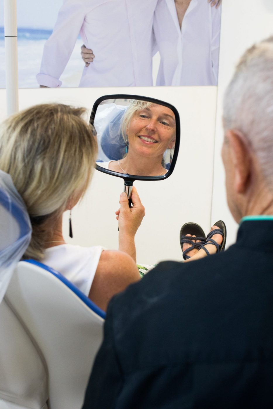 A patient in the treatment chair checking her smile in a hand mirror
